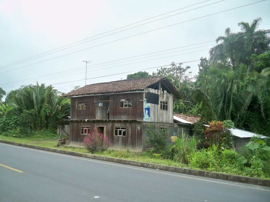 Cycling past a ramshackle two storey board house in Ecuador