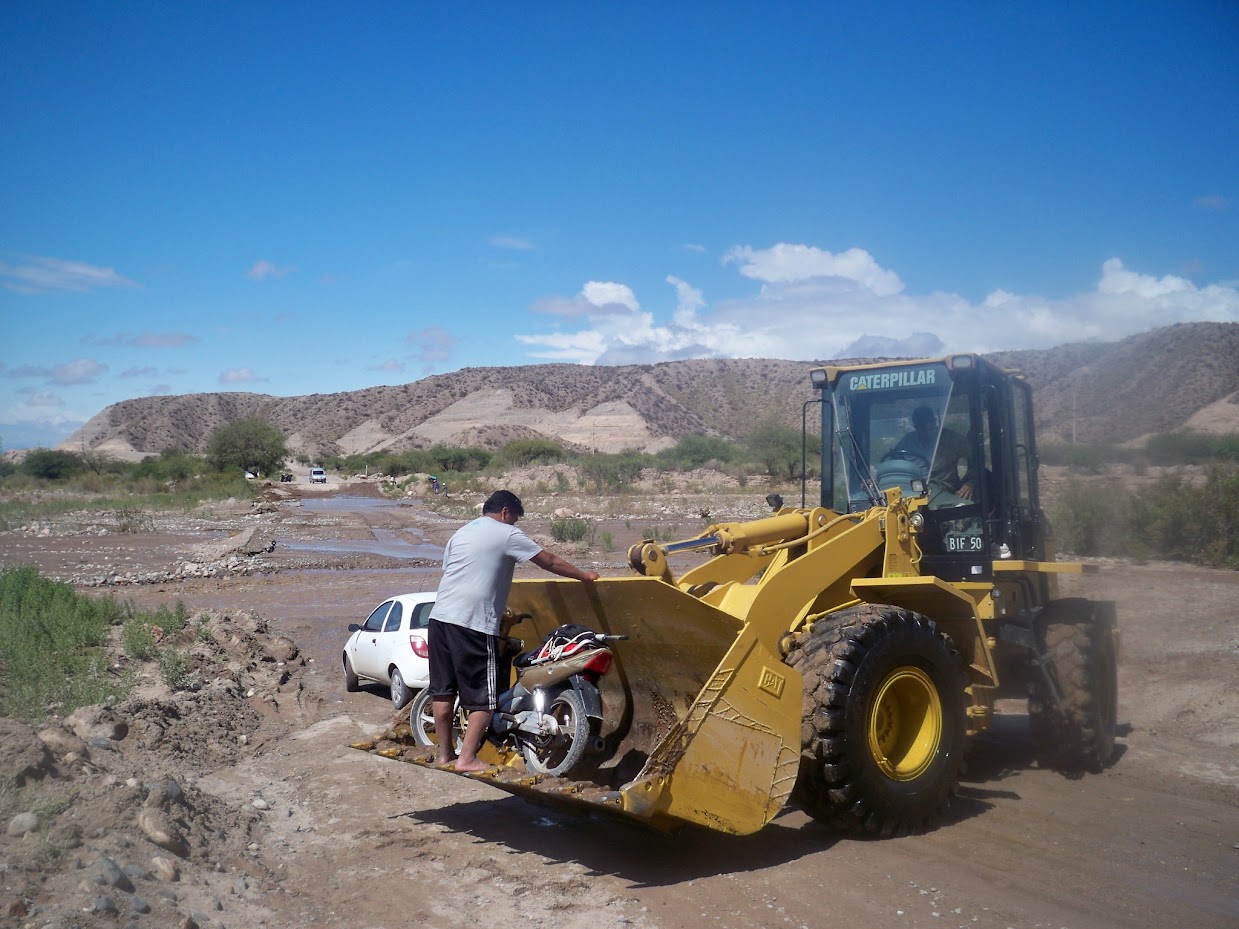 A moped crossing the river in the bucket of a tractor