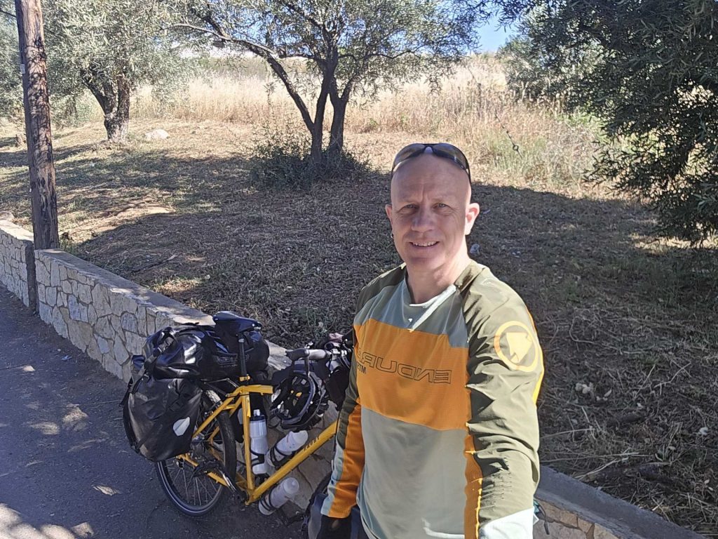 Standing with my fully loaded Thorn Nomad Mk2 yellow touring bicycle on a roadside among olive trees in the Greek countryside